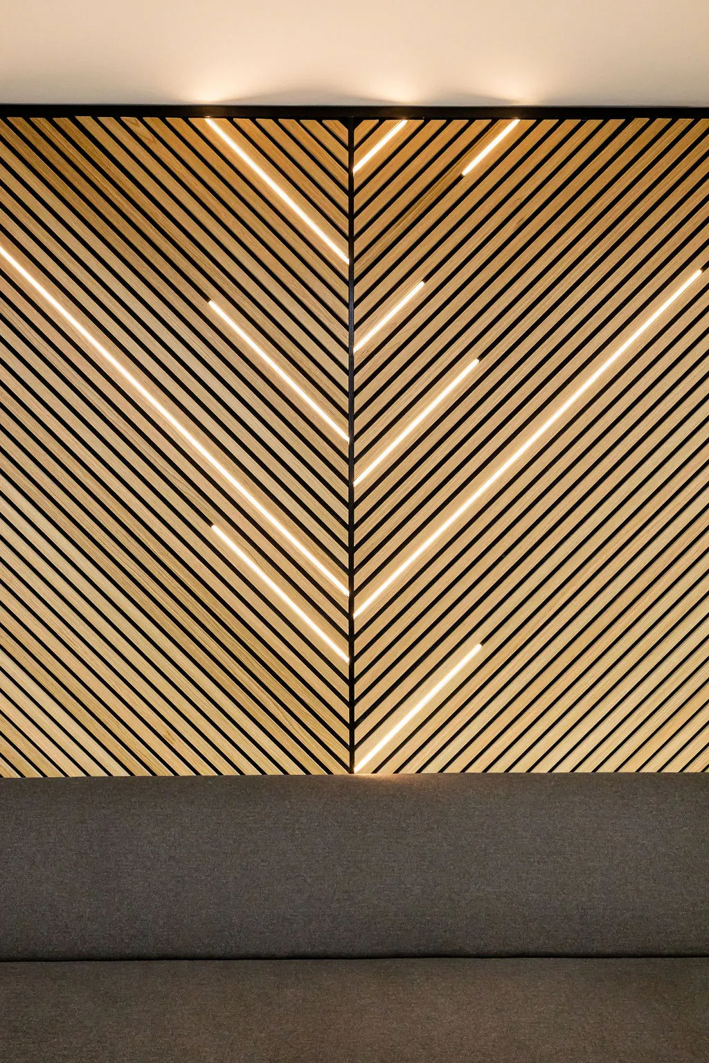 Backlit chevron acoustic wall panels in natural wood-look slats